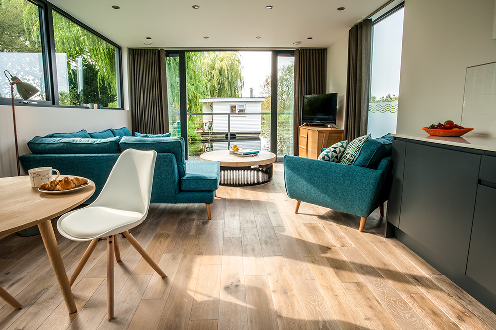 Photo of the living room on a luxury houseboat, with a view to the water and trees outside.