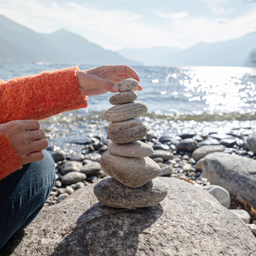 Close up of woman's hand stacking rocks in front of a lake