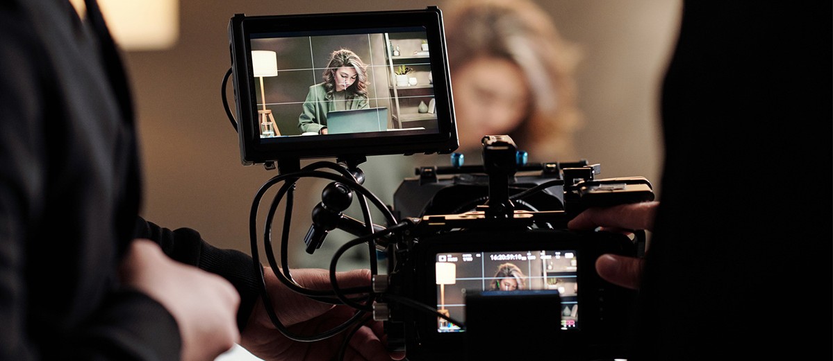 Close-up of steadicam screens with female model using laptop by table