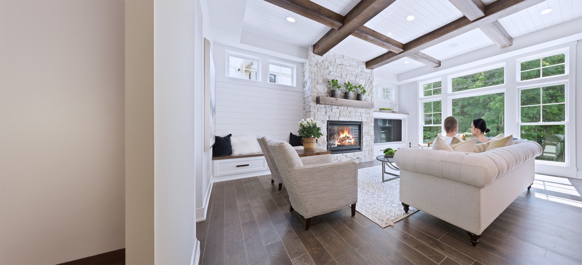 Couple sat on sofa in luxurious white living room with fireplace and large windows